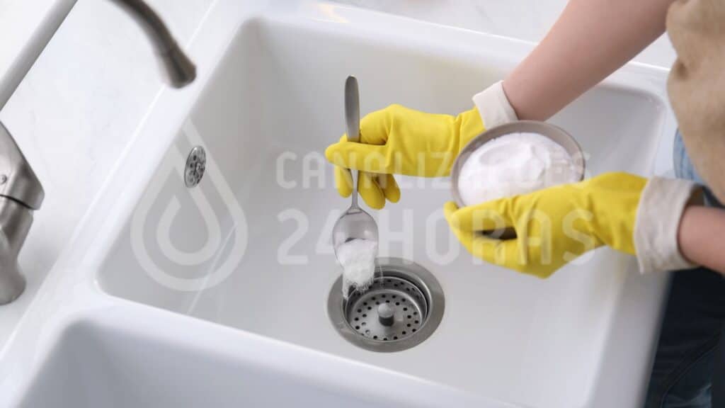 Pessoa com luvas de proteção a manusear soda cáustica perto de um ralo no lava-loiça